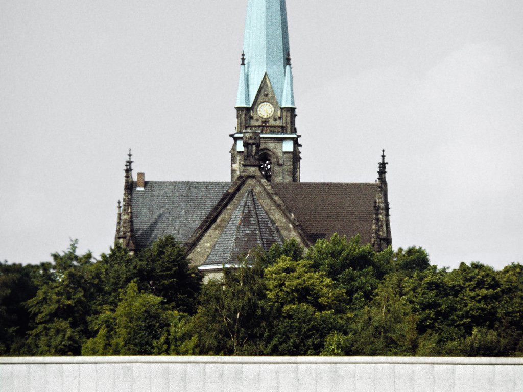 Blick über das frühere Bahnhofsgelände am Nordbahnhof, hinter der äußeren Mauer die St.-Sebastian-Kirche in der Gartenstraße im West-Berliner Bezirk Wedding; Aufnahme 1. Juni 1990  Auf dem Grenzstreifen im Vordergrund blühen gelbe Lupinen. Dahinter ist ein Stück Berliner Mauer zu sehen und im Hintergrund steht die Sanktsebastiankirche.