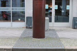 The bronze-coloured memorial column for Peter Fechter. In front of it is a line of bricks representing the path of the former Berlin Wall and a round granite plate.