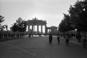 Das Brandenburger von der Straße Unter den Linden in Richtung Tiergarten fotografiert. Dutzende von Menschen sind zu Fuß oder auf dem Fahrrad unterwegs.