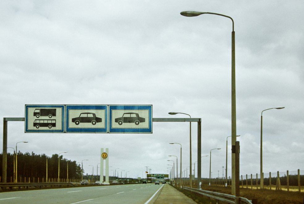 Autobahn A111 mit Blick auf Schilder zur Verkehrsregelung, Lampenmasten und Hoheitszeichen der DDR des Grenzübergangs Stolpe; Aufnahme 15. April 1990