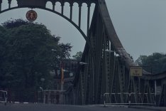 Nahaufnahme der Brücke. Das DDR-Emblem ist in der Mitte zu erkennen. Im Vordergrund sieht man die Grenzsperren und ein Schild mit der Aufschrift Potsdam.