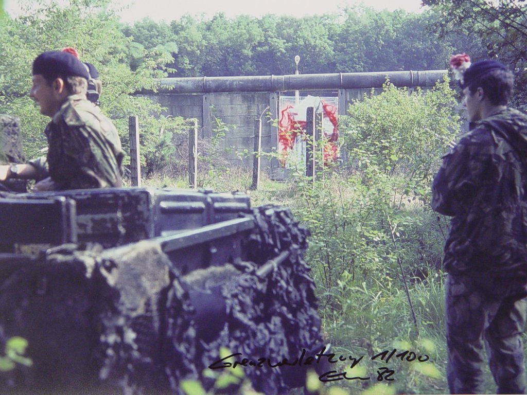 Im Vordergrund ist ein Militärfahrzeug zu sehen und zwei Soldaten. Im Hintergrund die Mauer mit Elsners Bild.