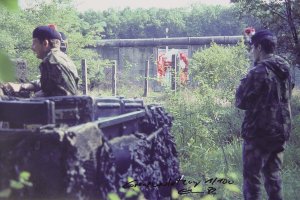 Im Vordergrund ist ein Milit&auml;rfahrzeug zu sehen und zwei Soldaten. Im Hintergrund die Mauer mit Elsners Bild.