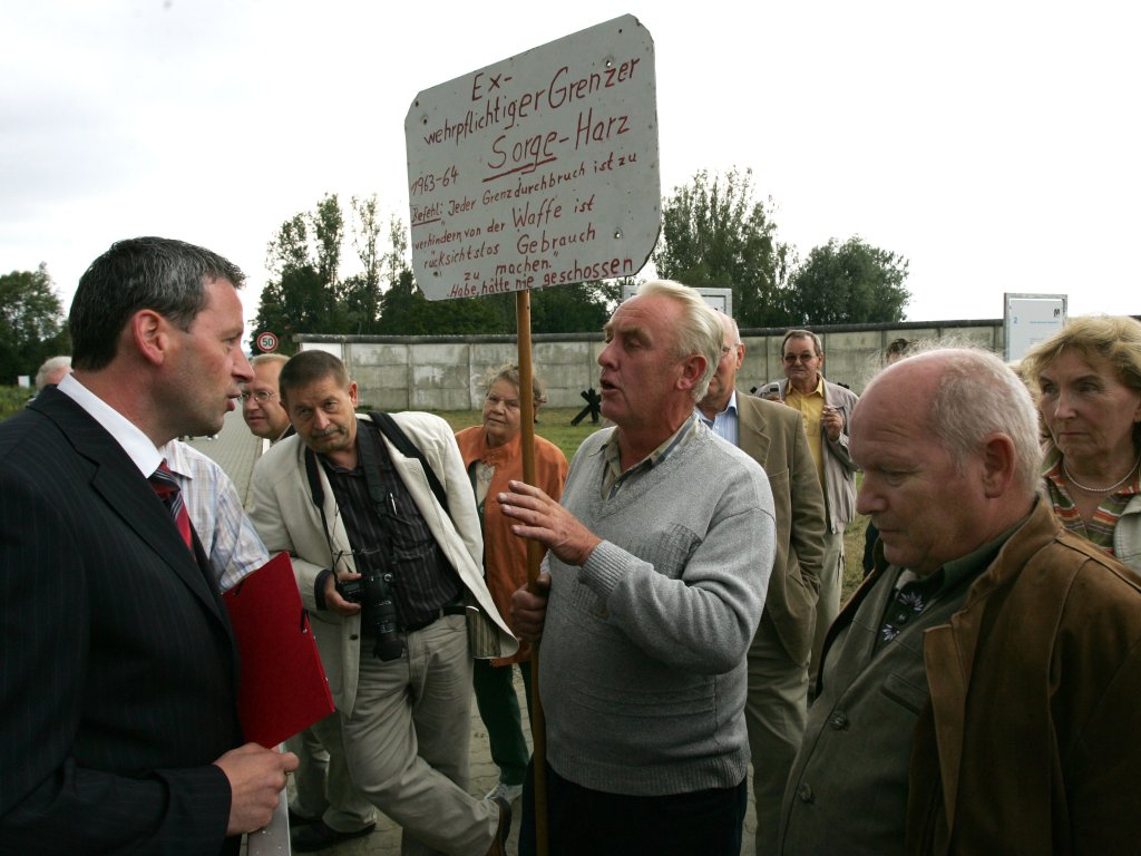 2006: Bei einer Gedenkveranstaltung im Grenzmuseum in Hötensleben zum 45. Jahrestag des Mauerbaus hält ein ehemaliger Grenzsoldat ein Schild, auf dem zu lesen ist: „Ex-wehrpflichtiger Grenzer 1963-64 Sorge-Harz. Befehl: ‚Jeder Grenzdurchbruch ist zu verhindern, von der Waffe ist rücksichtslos Gebrauch zu machen.‘ Habe, hätte nie geschossen.“.