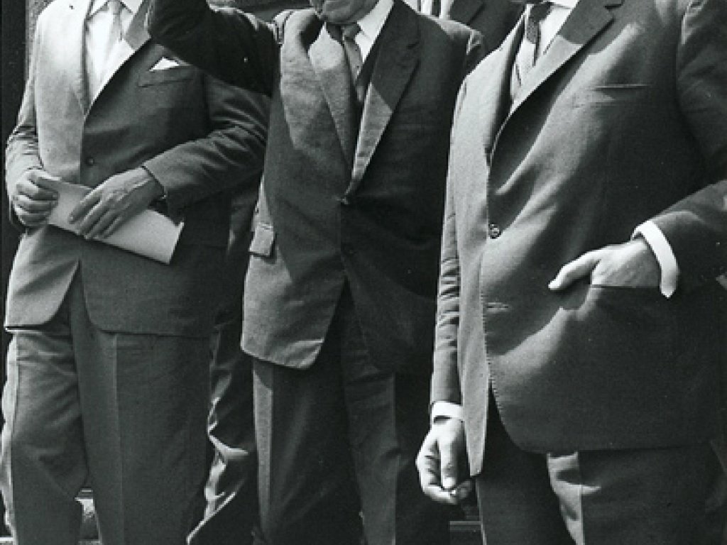 Willy Brandt geht rechts im Vordergrund eine Treppe hinunter. Neben ihm wirft Adenauer den Arm gestikulierend in die Luft. Daneben und dahinter gehen weitere Männer.