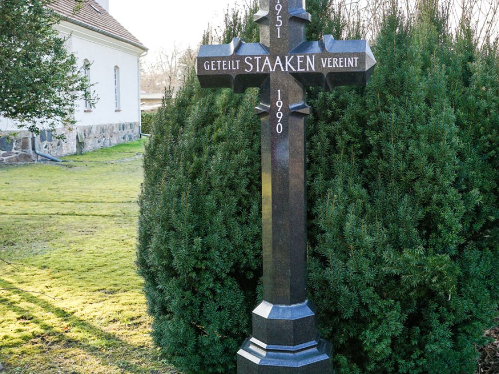 Granitkreuz zur Erinnerung an die von 1951 bis 1990 währende Teilung Staakens an der Dorfkirche in Alt-Staaken, errichtet im Jahr 2000; Aufnahme 2015  Granitkreuz zur Erinnerung an die von 1951 bis 1990 währende Teilung Staakens an der Dorfkirche in Alt-Staaken, errichtet im Jahr 2000; Aufnahme 2015