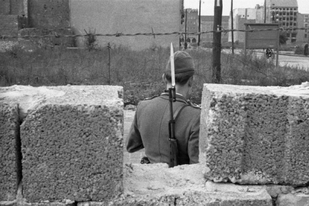 Durch eine L&uuml;cke zwischen Hohlblockmauersteinen ist der R&uuml;cken eines Soldaten zu sehen.