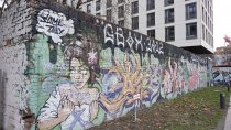 The graffiti covered breeze block wall. Over the back end of the wall, a newly constructed building overhangs.