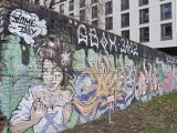 The graffiti covered breeze block wall. Over the back end of the wall, a newly constructed building overhangs.