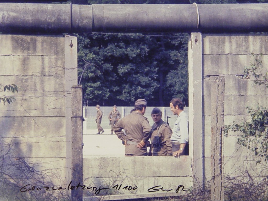 Nahaufnahme der Mauer. Im Zentrum die herausgebrochene Lücke, durch die vier Grenzsoldaten und ein Mann in Zivil zu sehen sind.