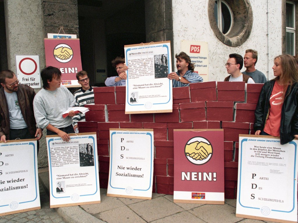1994: Fünf Jahre nach der Friedlichen Revolution protestieren Mitglieder der Jungen Union Thüringen am Jahrestag des Mauerbaus vor der PDS-Landesstelle in Erfurt. Die PDS ist aus der SED hervorgegangen und hat sich 2007 zusammen mit der WASG zur heutigen Partei Die Linke formiert.
