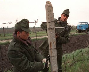 Zwei Soldaten stehen links und rechts von einem Betonpfeiler und durchschneiden mit Bolzenschneider und Kneifzange den Stacheldraht.