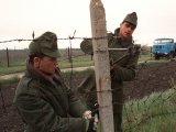 Zwei Soldaten stehen links und rechts von einem Betonpfeiler und durchschneiden mit Bolzenschneider und Kneifzange den Stacheldraht.