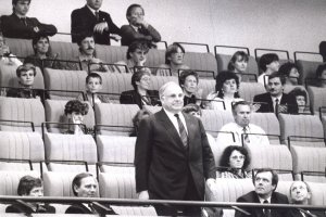 Die Sitze der Gästetribüne der Volkskammer sind zum Großteil belegt. In der vordersten Reihe steht Helmut Kohl, einige der um ihn Sitzenden schauen zu ihm auf.
