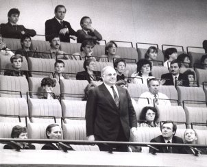 Die Sitze der Gästetribüne der Volkskammer sind zum Großteil belegt. In der vordersten Reihe steht Helmut Kohl, einige der um ihn Sitzenden schauen zu ihm auf.