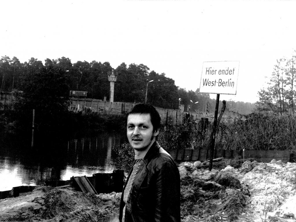 Im Vordergrund steht Hartmut Richter und blickt in die Kamera, hinter ihm steht ein Schild mit der Aufschrift: Hier endet West-Berlin. Im Hintergrund verlaufen der Kanal und die Mauer. Am anderen Ufer ist ein Wachturm zu erkennen.