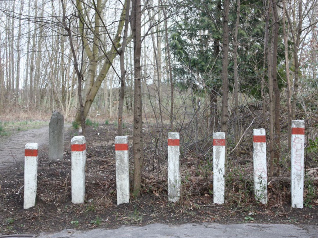 West-Berliner Grenzmarkierungspfosten (links hinten) und Pfostensperre am Gedenkkreuz für Horst Kullack, der am 1. Januar 1972 bei einem Fluchtversuch angeschossen wurde und am 21. Januar 1972 seinen Verletzungen erlag, in der Wittelsbacher Straße in Berlin-Lichtenrade; Aufnahme 2015