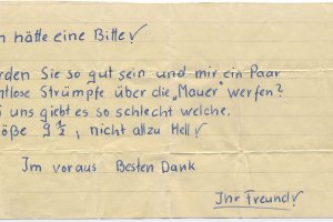 "Ich hätte eine Bitte! Würden Sie so gut sein und mir ein Paar nahtlose Strümpfe über die "Mauer" werfen? Bei uns gibt es so schlecht welche. Größe 9 1/2, nicht allzu hell! Im Voraus Besten Dank. Ihr Freund!"