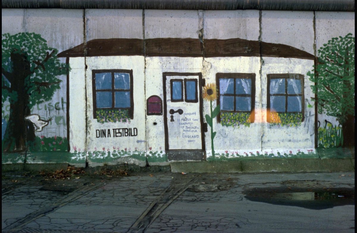 Ein über mehrere Mauersegmente gemaltes Bild zeigt ein weißes Haus zwischen zwei Bäumen. Das Haus hat eine Tür, drei Fenster und einen Briefkasten. Unter dem Fenster links steht: Din A Testbild. Neben der Tür ist eine Sonnenblume gemalt. Ein über mehrere Mauersegmente gemaltes Bild zeigt ein weißes Haus zwischen zwei Bäumen. Das Haus hat eine Tür, drei Fenster und einen Briefkasten. Unter dem Fenster links steht: Din A Testbild. Neben der Tür ist eine Sonnenblume gemalt.