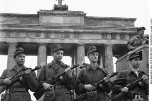 Dieses Foto vom 14. August 1961 dient der SED-Propaganda als visuelles Gegenst&uuml;ck zu den vom Westen verbreiteten Aufnahmen der Mauer &ndash; wie dem &bdquo;Sprung in die Freiheit&ldquo; von Conrad Schumann. Die Aufnahme der vier M&auml;nner vor dem Brandenburger Tor soll den Mauerbau als Ma&szlig;nahme zur &bdquo;Friedenssicherung&ldquo; legitimieren. Es soll eine &bdquo;menschliche Mauer&ldquo; zeigen, eine Schutz- und Verteidigungsgeste gegen den Westen.