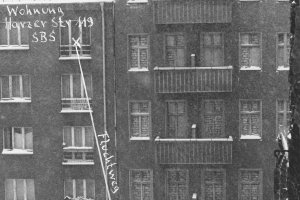 Frontalaufnahme von zwei aneinandergebauten Wohnhäusern. Die Fenster des rechten Hauses sind zugemauert. Am unteren Bildrand trennt eine Mauer die Fläche vor den Häusern. Neben einem Fenster im vierten Stock des linken Hauses ist handschriftlich notiert: Wohnung Harzer Str 119 SBS. Von hier führt ein Pfeil mit der Beschriftung: Fluchtweg schräg nach unten rechts, wo steht: Aufsprung auf Westberliner Gebiet.