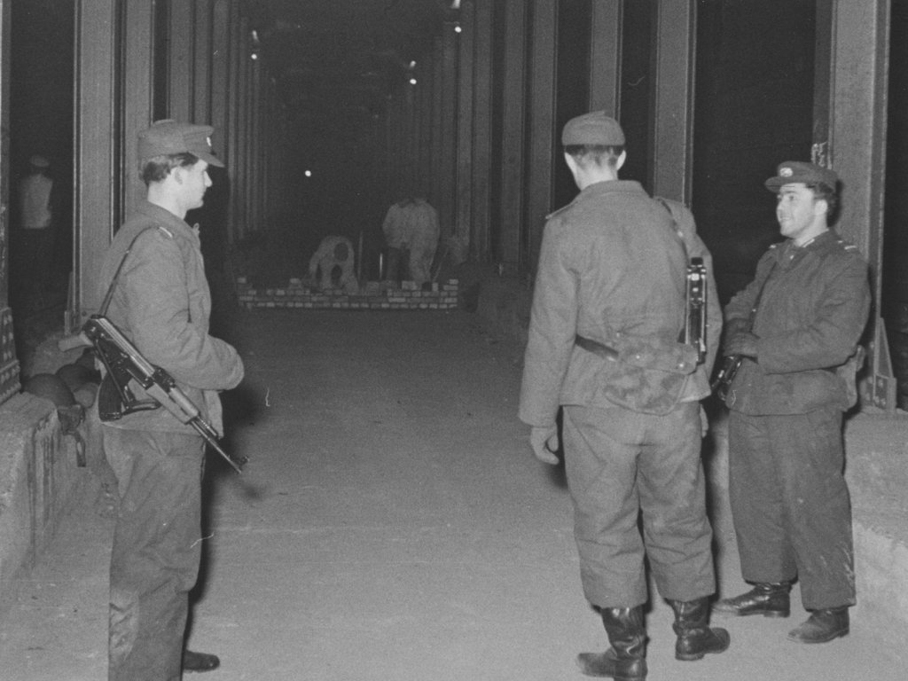 Border soldiers guard  bricklayers who are putting up a barrier wall between the Heinrich-Heine-Strasse and Moritzplatz underground railway stations, 15 Februar 1963