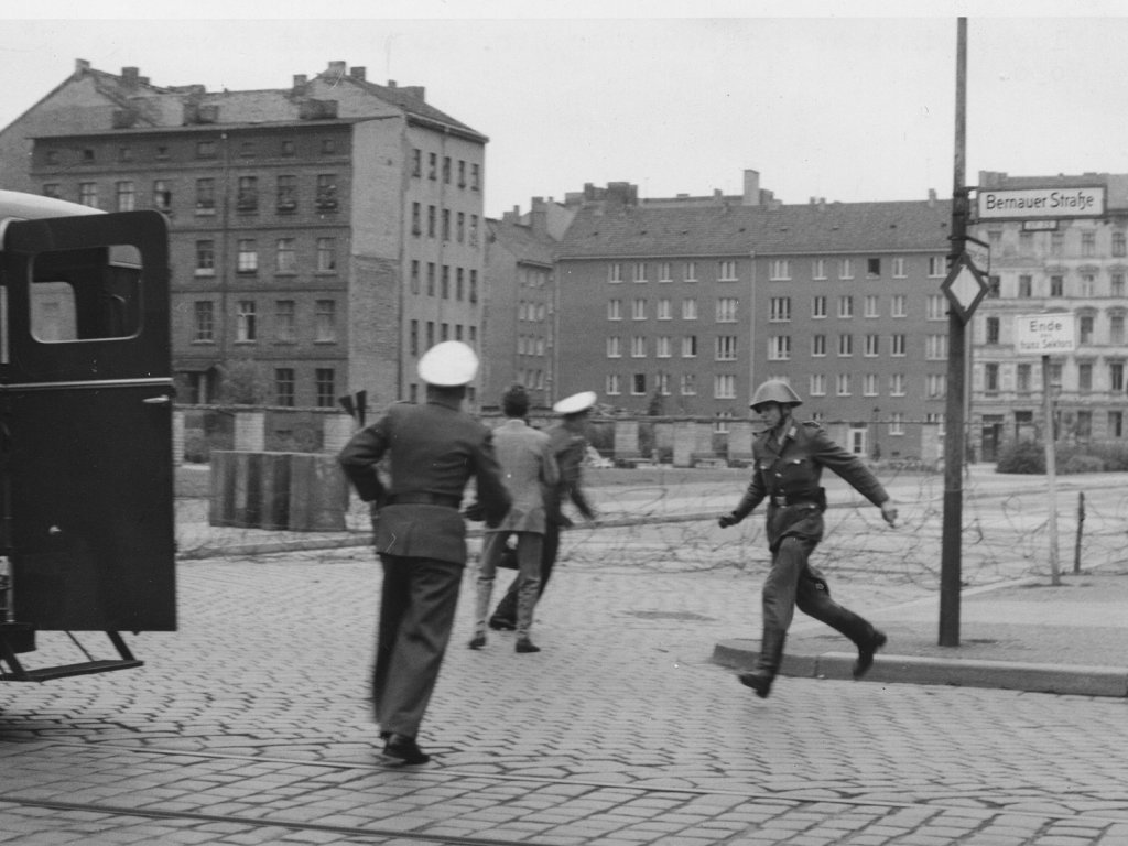 „Sprung in die Freiheit“, Bernauer Straße, 15. August 1961: Der DDR-Grenzpolizist Conrad Schumann rennt nach seinem Sprung zu einem Streifenwagen der West-Berliner Polizei. Zwei Beamte bergen seine Waffe