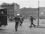 „Sprung in die Freiheit“, Bernauer Straße, 15. August 1961: Der DDR-Grenzpolizist Conrad Schumann rennt nach seinem Sprung zu einem Streifenwagen der West-Berliner Polizei. Zwei Beamte bergen seine Waffe