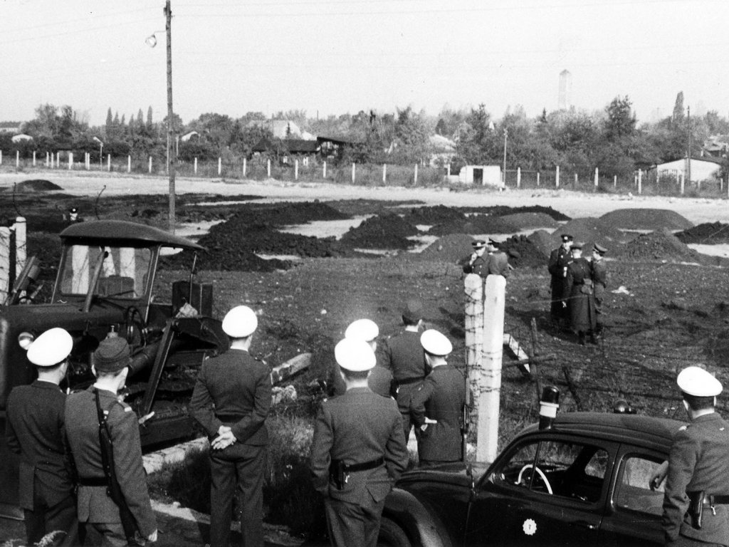 West-Berliner Schutzpolizisten und Ost-Berliner Grenzsoldaten stehen sich am Fluchtort gegenüber: Gelungene Flucht eines Grenzpolizisten mit einer Raupe, 18. Oktober 1963