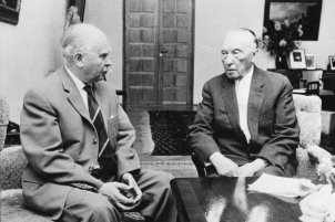 Kroll und Adenauer sitzen auf Sesseln an einem niedrigen Tisch und unterhalten sich mit ernster Miene.