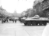 Im Vordergrund fährt ein Panzerwagen über die Straße. Er trägt eine Markierung mit der Zahl 231. Die Straße ist voller Menschen, die in Richtung des Militärfahrzeugs blicken. Im Hintergrund sind der Prager Wenzelsplatz und das Nationalmuseum zu erkennen.