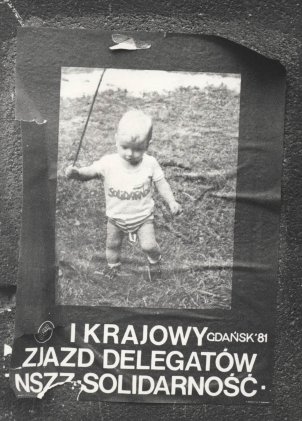 An einer Wand klebt ein Solidarnosc-Flyer. Darauf ist ein Foto von einem Kleinkind abgebildet. Es trägt ein T-Shirt, das mit dem Solidarnosc-Logo bedruckt ist. Unter dem Foto steht der Aufruf zum Kongress in polnischer Sprache.