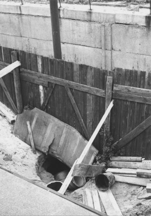 Direkt an der Mauer klafft ein Loch im Boden. Rundherum liegen Bretter und leere Eimer.