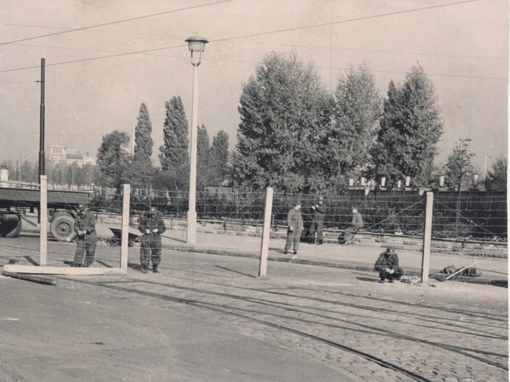 Im Grenzstreifen errichten Grenzsoldaten Stacheldrahtzäune. Auf der Fahrbahn sind noch die Staßenbahngleise zu erkennen, im Hintergrund ein Zaun der an das Gebäude des ehemaligen Preußischen Landwirtschaftsministeriums an der Stresemannstraße grenzt.