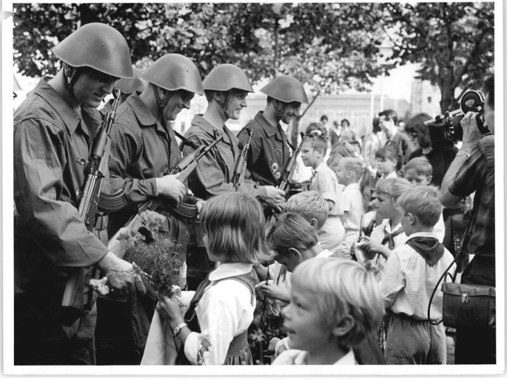 1966: Junge Pioniere überreichen den Grenzbrigaden am 13. August 1966 Blumen. Die DDR-Jugendorganisationen sind jeweils stark involviert in die staatlich organisierten Feierlichkeiten. Die dankbare, zusammenstehende Gemeinschaft ist in der DDR-Berichterstattung ein wiederkehrendes Motiv.