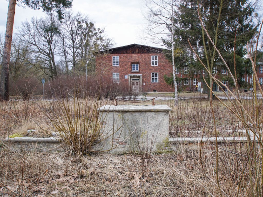 Überwuchertes Denkmal und Kasernengebäude des DDR-Grenzregiments 34 in Groß Glienicke (ehem. Rosa-Luxemburg-Kaserne); Aufnahme 2015  Überwuchertes Denkmal und Kasernengebäude des DDR-Grenzregiments 34 in Groß Glienicke (ehem. Rosa-Luxemburg-Kaserne); Aufnahme 2015