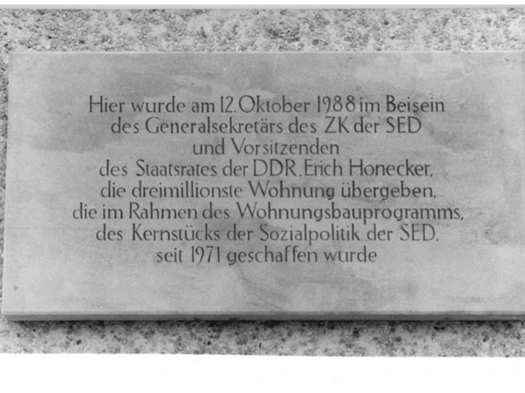 Steinplakette mit der Inschrift: Hier wurde am 12. Oktober 1988 im Beisein des Generalsekretärs des ZK der SED und Vorsitzenden des Staatsrates der DDR, Erich Honecker, die dreimillionste Wohnung übergeben, die im Rahmen des Wohnungsbauprogramms, des Kernstücks der Sozialpolitik der SED, seit 1971 geschaffen wurde.