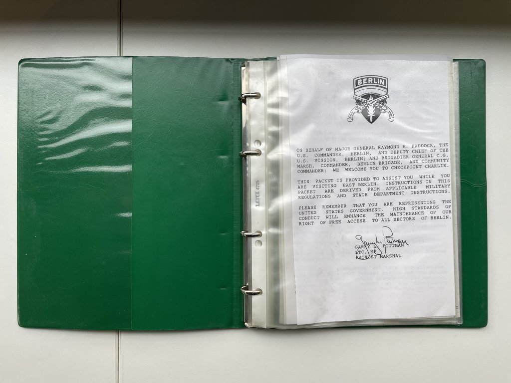 Auf dem Bild ist eines der „vehicle travel packets“ der US-Army zu sehen: ein grünes Ringbuch mit bedruckten Seiten in Klarsichtfolien. Aufgeschlagen ist die Titelseite. Diese enthält eine Begrüßung im Namen des US-Stadtkommandanten Major General Raymond E. Haddock, unterzeichnet von Provost Marshal Garry L. Pittman.