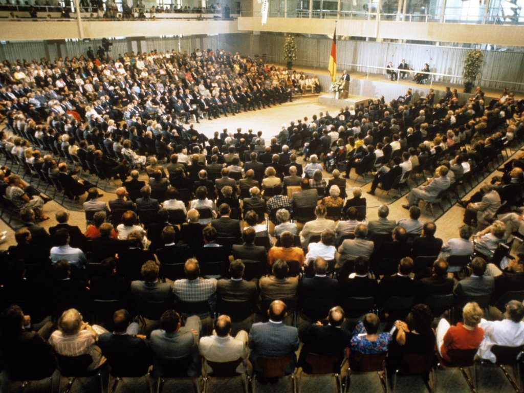 1986: Gedenkveranstaltung zum 25. Jahrestag des Mauerbaus im Reichstagsgebäude in West-Berlin. Trotz der Annäherung beider deutscher Staaten, sagt Bundeskanzler Helmut Kohl in seiner Rede: „Wir werden und dürfen uns nicht an dieses Monument der Unmenschlichkeit gewöhnen … Solange es Mauer, Stacheldraht und Schießbefehl gibt, kann von Normalität in Deutschland keine Rede sein.“.