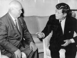 Links im Bild sitzt Nikita Chruschtschow, seine Hände liegen auf den Knien. Er schaut nach rechts zu John F. Kennedy, der gestikulierend auf ihn einredet.