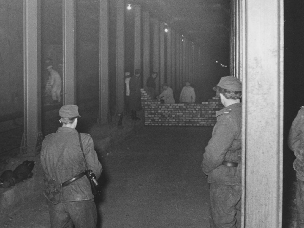 Border soldiers guard  bricklayers who are putting up a barrier wall between the Heinrich-Heine-Strasse and Moritzplatz underground railway stations, 15 Februar 1963