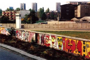 Im unteren Bildteil ist die bunt bemalte Mauer zu sehen. Dar&uuml;ber sieht man in den Grenzstreifen, wo ein Wachturm steht.