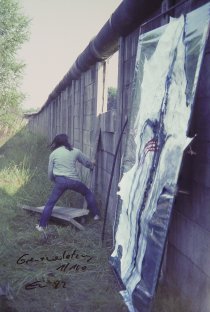 Elsner hebt quer montierte Betonteile aus der Mauer. Die drei obersten Elemente hat er bereits entfernt, zwei liegen am Boden, eins hält er noch in den Händen. Im Vordergrund steht sein Bild an die Mauer gelehnt.