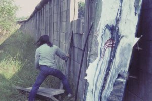 Elsner hebt quer montierte Betonteile aus der Mauer. Die drei obersten Elemente hat er bereits entfernt, zwei liegen am Boden, eins h&auml;lt er noch in den H&auml;nden. Im Vordergrund steht sein Bild an die Mauer gelehnt.