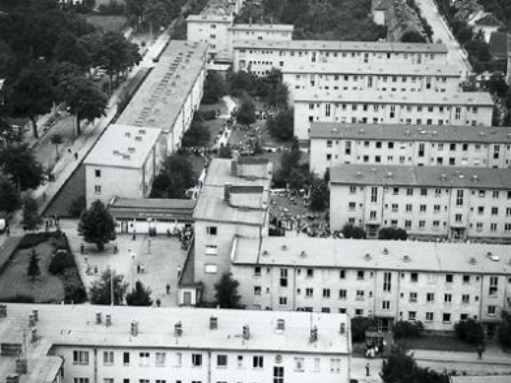 Luftaufnahme des Notaufnahmelagers. Es besteht aus mehreren, rechtwinklig zueinanderstehenden, dreigeschossigen Wohnblöcken mit Flachdächern.