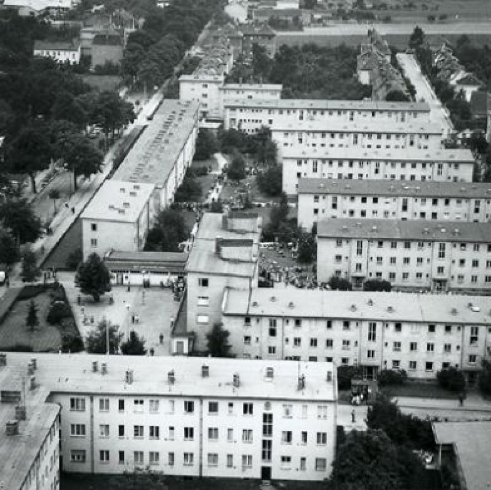 Luftaufnahme des Notaufnahmelagers. Es besteht aus mehreren, rechtwinklig zueinanderstehenden, dreigeschossigen Wohnblöcken mit Flachdächern.