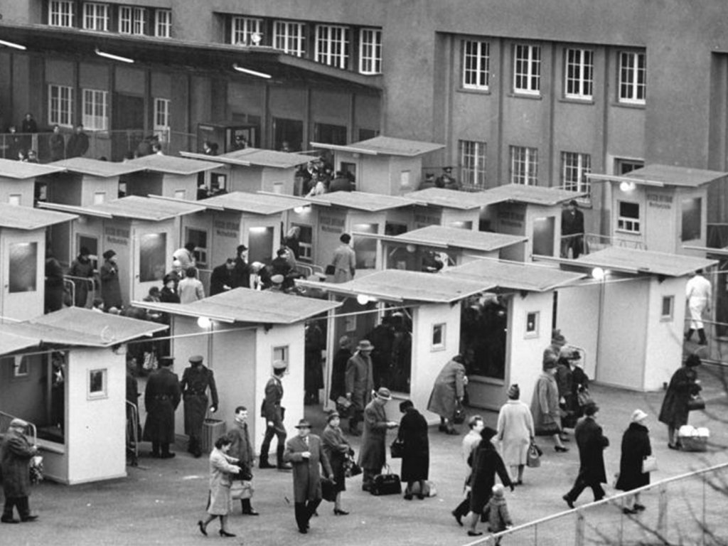 Vor dem Bahnhof stehen in mehreren Reihen zwanzig kleine Häuschen, darin und darum sind viele Menschen versammelt.