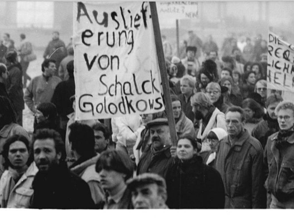 Einige Menschen in einer demonstrierenden Menschenmenge halten Transparente hoch. Auf dem größten in der Bildmitte wird gefordert: Auslieferung von Schalck-Golodowski.