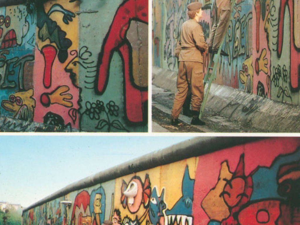 Das Bild besteht aus drei Fotos. Oben links sitzen vier Grenzsoldaten auf der Mauerkrone und halten eine Leiter, die auf der anderen Seite steht. Auf dem rechten Bild stehen drei Grenzsoldaten auf einer Leiter an der Mauer. Der mittlere fasst ein an der Mauer befestigtes Waschbecken von unten an. Auf dem unteren Bild stehen sie vor der Installation aus Waschbecken und Pissoir an der buntbemalten Mauer und fotografieren sie.