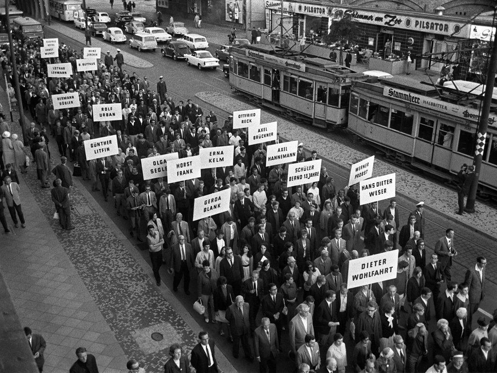 1965: Schweigemarsch zum 4. Jahrestag des Mauerbaus in der Berliner Kantstraße: Schilder mit den Namen der Mauertoten bedruckt, werden in die Höhe gehalten.
